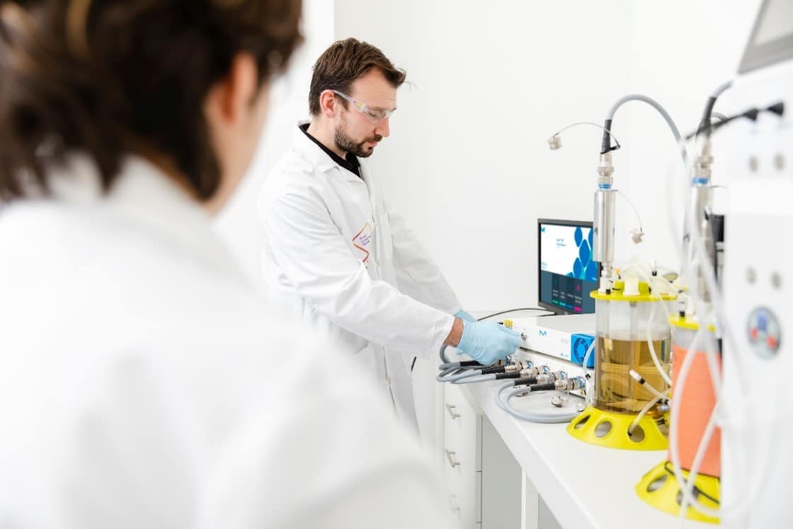 Two operators in a lab operating a Raman system to monitor upstream bioprocess CPPs and CQAs in-line and in real time.